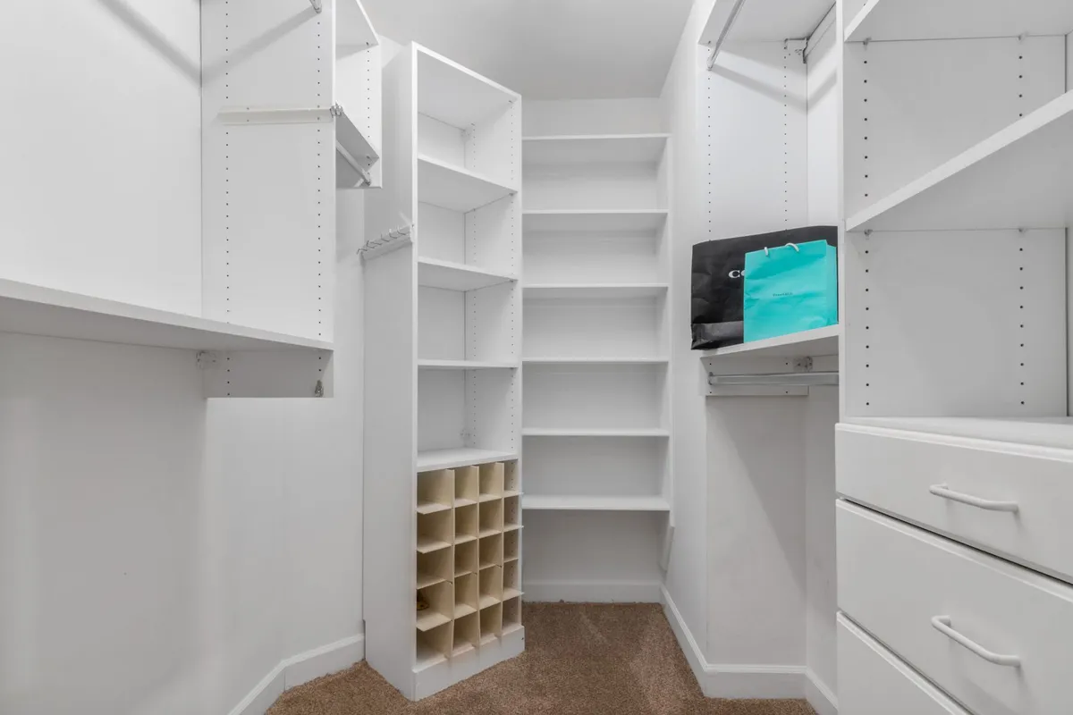 A white walk-in closet with double-hang sections, shoe cubbies and a stack of drawers
