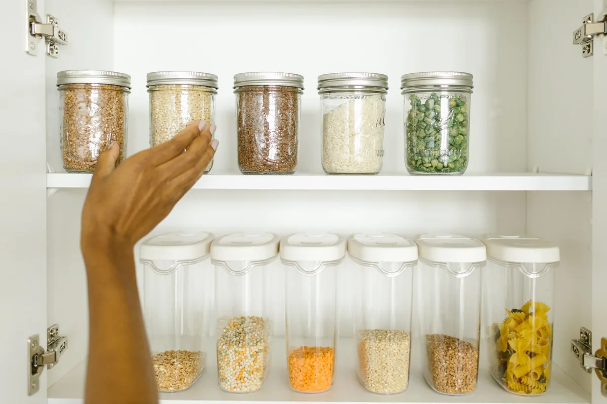 A hand reaching for a jar on a shallow white pantry shelf with concealed hinges visible in a Newport Beach CA kitchen