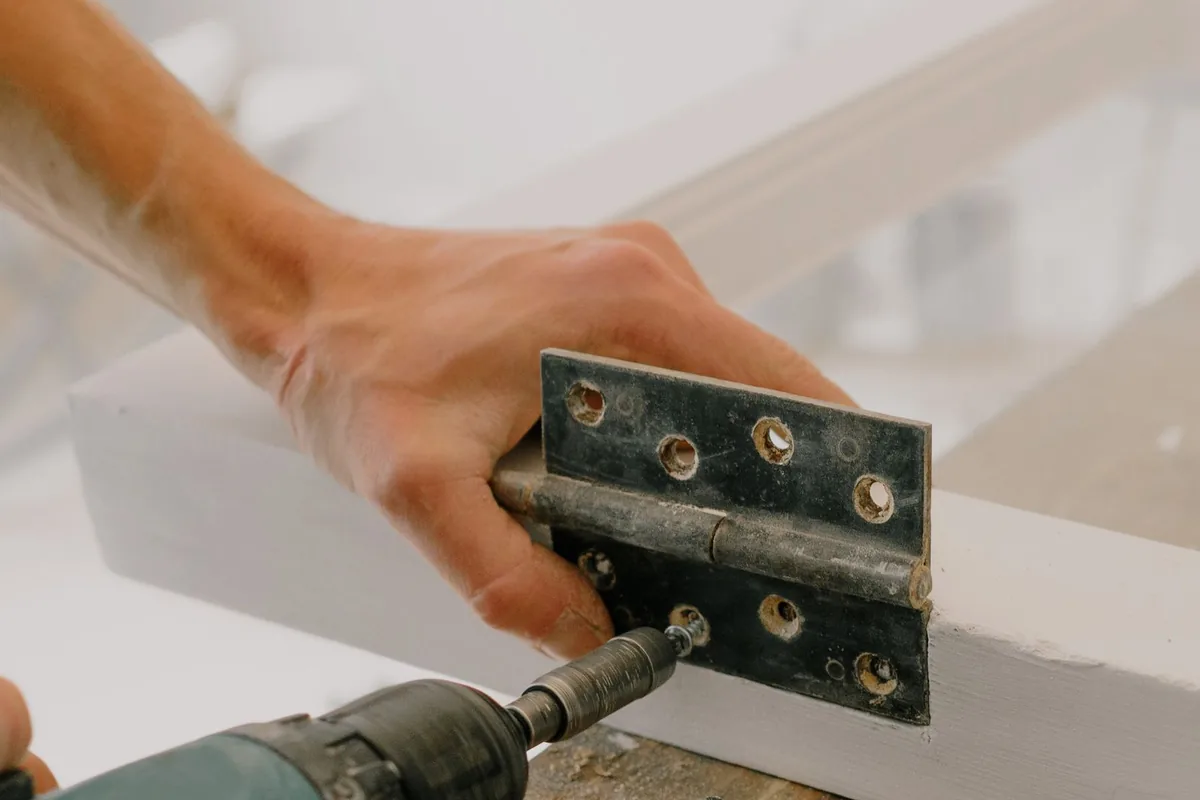 A hinge being driven into painted joinery with a cordless driver, a common cabinet repair in Newport Beach CA